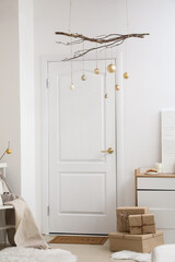 Tree branches with Christmas balls hanging near white door in room