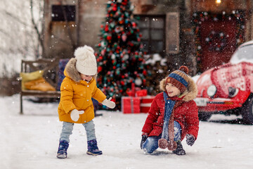 Children play outdoors in snow. Christmas and New Year tree and red retro car cozy background. Concept of childhood and happiness.