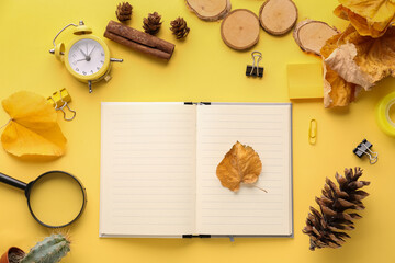 Fototapeta na wymiar Composition with blank notebook, stationery, alarm clock and autumn leaves on yellow background