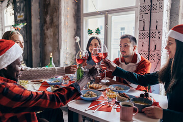 People celebrating sitting at the table, clinking glasses. Christmas or New Year eve. - obrazy, fototapety, plakaty