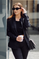 Obraz premium Outdoors lifestyle portrait of stunning brunette girl. Drinking coffee and walking on the city street.