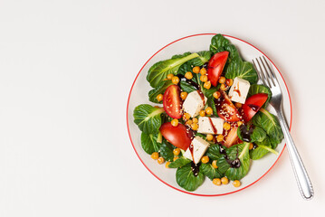 Fresh pak choi salad with tomatoes, chickpeas and feta cheese toping with sauce and sesame seeds in a plate with a fork isolated on white background with copy space