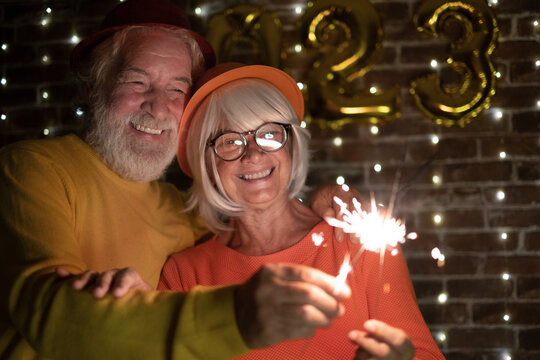 Beautiful Caucasian Senior Couple Holding Sparklers Celebrating New Year. Happy Lifestyle For Mature Retirees, Party Lights