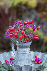 Blumenstrauß mit Hagebutten und Liebesperlenstrauch-Früchten im vintage Krug im Garten