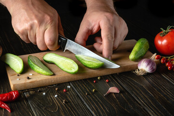 The cook cuts fresh cucumbers for pickling with spices and vegetables. Close-up of a chef hands while working on a kitchen table in a restaurant