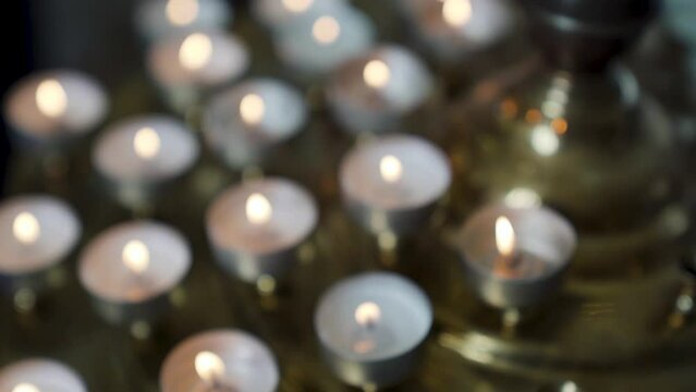Yellow candle in front with many out of focus candles in background of church