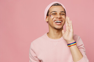 Young promoter gay man wears sweatshirt hat scream hot news about sales discount hold hand near mouth isolated on plain pastel light pink color background studio portrait Lifestyle lgbtq pride concept