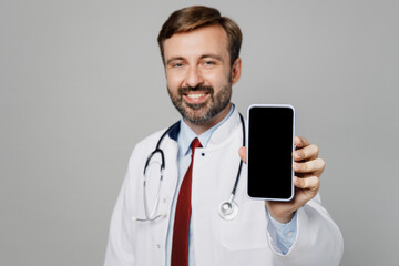 Male doctor man wears white medical gown suit stethoscope work in hospital use show close up mobile cell phone blank screen area isolated on plain grey color background. Healthcare medicine concept.