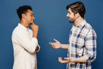 Sideways young two friends smiling happy cheerful fun cool men 20s wear white casual shirts talk speak together isolated plain dark royal navy blue background studio portrait People lifestyle concept.