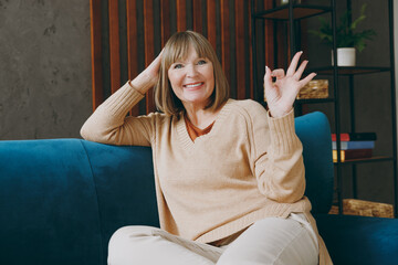 Elderly smiling cheerful fun woman 50s years old wearing casual clothes sitting on blue sofa...