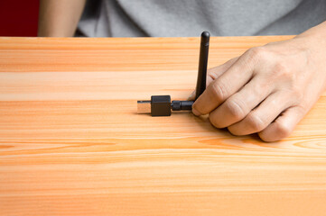 Black usb wifi placed on wooden floor, hand holding usb wifi