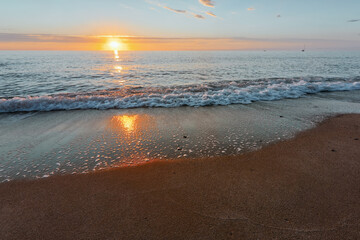 Sunrise on the seashore on the Italian Riviera. Sandy beach and waves reflecting the sunlight in the foreground. Vacation travel holiday banner, summer mood. The Ligurian Sea, Italy