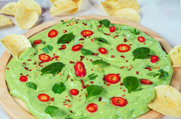 creamy avocado board with chili peppers, herbs and nachos Selective focus with blurred foreground and background