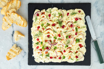 Flat lay of a butter board topped with red onions, dill leaves and micro green. Table top view