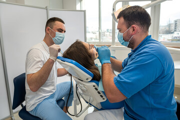 Pretty female patient sitting in armchair while doctor with assistant examining her teeth