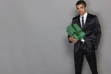 A man in a formal suit with a tie holds a box with a gift. Isolated on grey. Holiday concept.