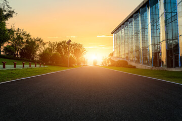 Asphalt road and glass wall building with forest at sunset