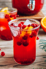 Christmas cranberry punch with oranges in a pitcher and glasses on rustic wooden table.