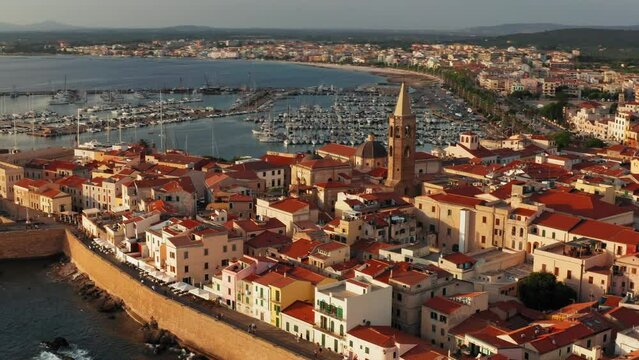 Cinematic shot of the old town of Alghero, Sardinia - Italy.
Drone view of ancient Italian city at Sunset. Golden hour, warm colors, view of the harbor in the distance.