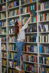 Young librarian searching for a book on bookshelves