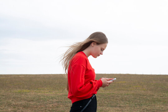 Teenage girl with red sweater text messaging in field