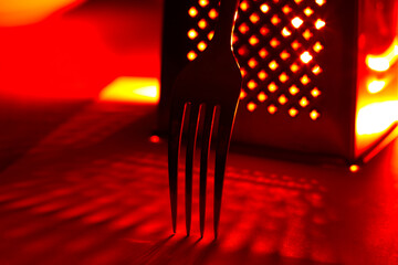 Fork and grater in the kitchen under red light. Concept for restaurants, bar, eating, kitchen. 