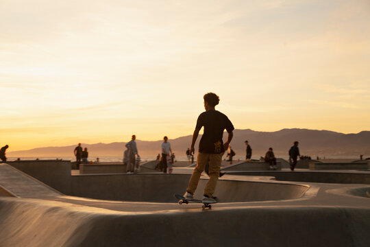 Teenage boy skating at skatepark during sunset