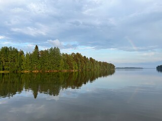 Forest trees reflection on the lake surface, lake mirror, quiet peaceful atmosphere, cloudy blue sky