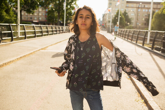 Girl holding smartphone while walking on bridge