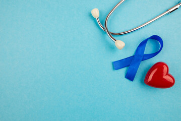 Top view photo of stethoscope and blue ribbon with small red heart, prostate cancer awareness symbol