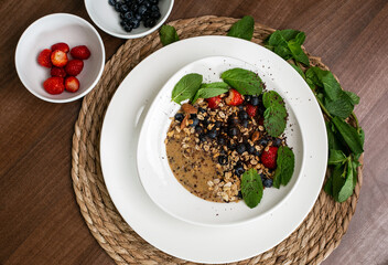 porridge with quinoa, chia, berries and nuts, mints on a white large plate stands on a brown table
