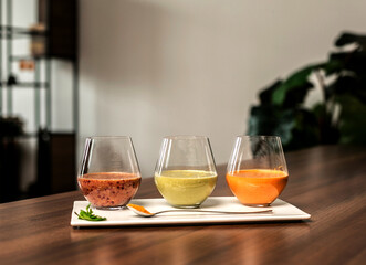 three glasses of smoothie with fruits and berries stand on a brown table with a spoon with turmeric