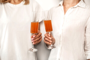 Two woman in white shirts are holding a glass with apple juice  