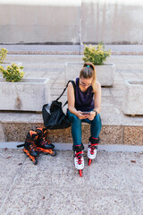 young blonde girl getting ready to go out on inline skates by looking at her mobile phone.