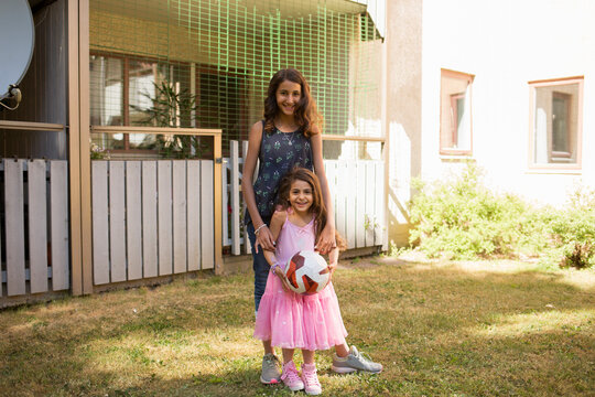 Smiling sisters playing with ball in backyard
