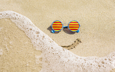 Sunglasses lie on the beach next to the sea. A smile is drawn under the glasses. The wave washes away the smile.
