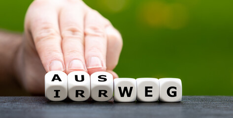 Hand turns dice and changes the German word 'Irrweg' (wrong way) to 'Ausweg' (way out).