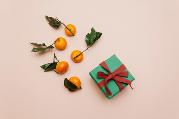 tangerines with green leaves, lying on a beige pastel background next to a green gift box. Preparation for the new year, copy space, top view. Flatlay