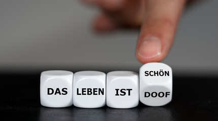 Concept to change the attitude. Hand turns dice and changes the German expression 'das Leben ist doof' (life is bad) to 'das Leben ist schön' (life is beautiful).