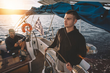 Young man at the sailboat helm  - obrazy, fototapety, plakaty