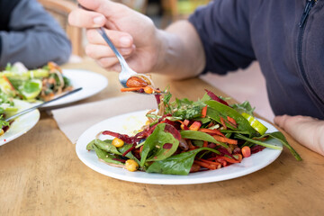 Green raw salad on a plate and man's hand with fork in it. 