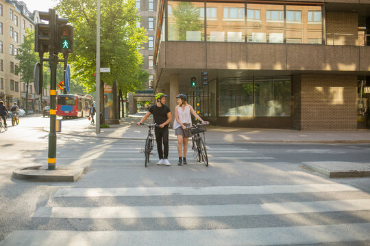 Young man and woman walking bicycles on pedestrian crossing