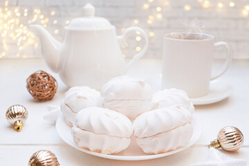  Winter, Christmas, New Year decoration composition, concept, background. White Mug, cup of hot tea, coffee, meringue, knitted plaid. Christmas lights. Christmas mood morning. Xmas greeting card.