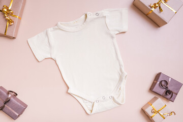 Baby t-shirt mockup for logo, text or design on beige background with gift boxes decorations top view