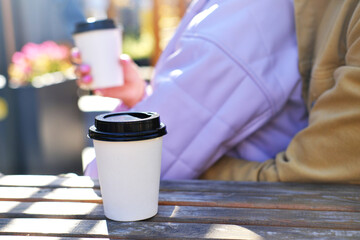 A paper cup with takeaway coffee stands on the table. Couple in love drinking hot drink on a date