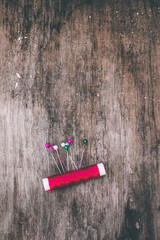 Red thread and colorful pins against an old wooden background