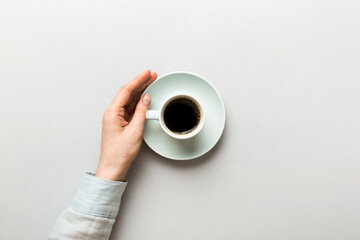 Minimalistic style woman hand holding a cup of coffee on Colored background. Flat lay, top view cappuccino cup. Empty place for text, copy space. Coffee addiction. Top view, flat lay