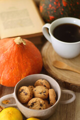 Cup of tea or coffee, seasonal spices, bowl of cookies, blanket, pumpkins, colorful leaves, books and tangerines on wooden table. Cozy hygge at home. Selective focus.