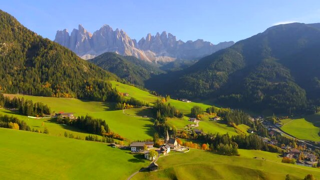 Wide drone footage of Chiesa di Santa Maddalena church in Italian Dolomites in European Alps. Footage of a small village, mountains, nature, grass fields, forest and hills. Filmed with a drone in 4k.