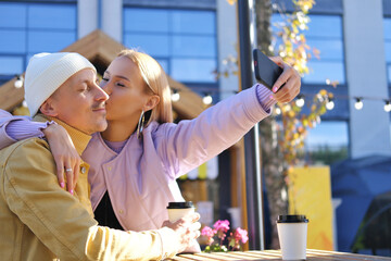 A blonde girl holds a phone and takes a selfie with her boyfriend. Girl kissing a guy
